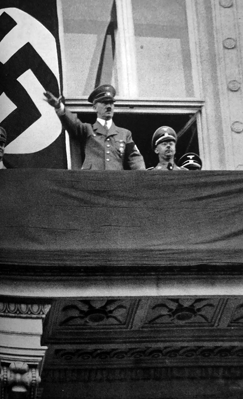 Adolf Hitler greets the crowd from the balcony of Hotel Imperial in Vienna, with Heinrich Himmler behind him